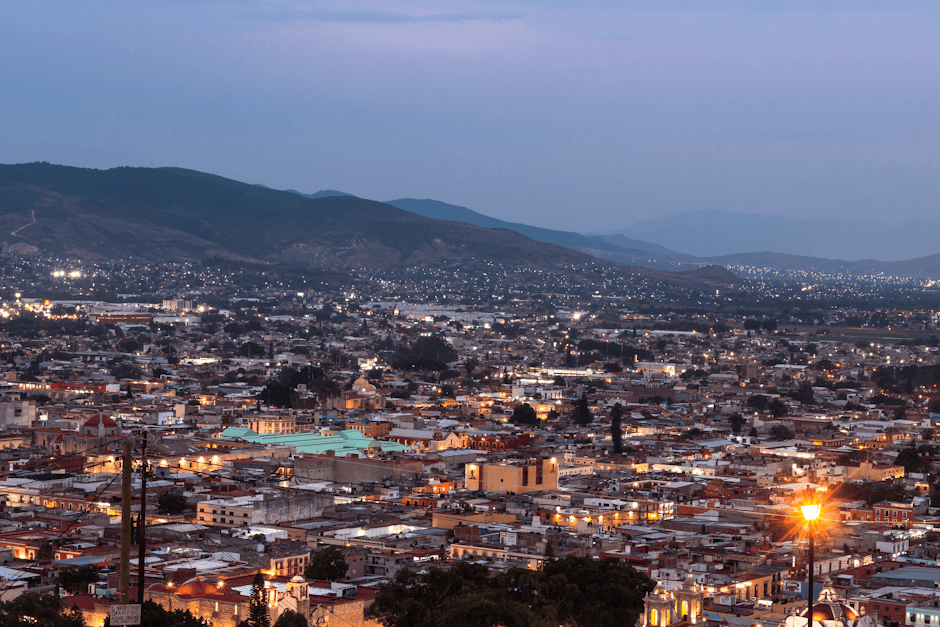 Beautiful cityscape at dusk featuring luminous city lights against a mountainous backdrop.