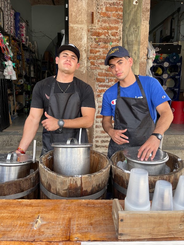 Heladería Los Güeros con vitrina de helados de colores y un cliente disfrutando un tejuino bajo luces nocturnas