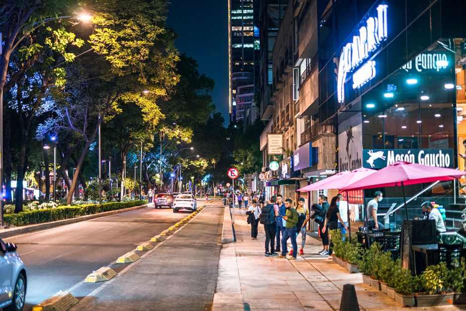 Lively street scene in Mexico City featuring people, restaurants, and illuminated storefronts at night.